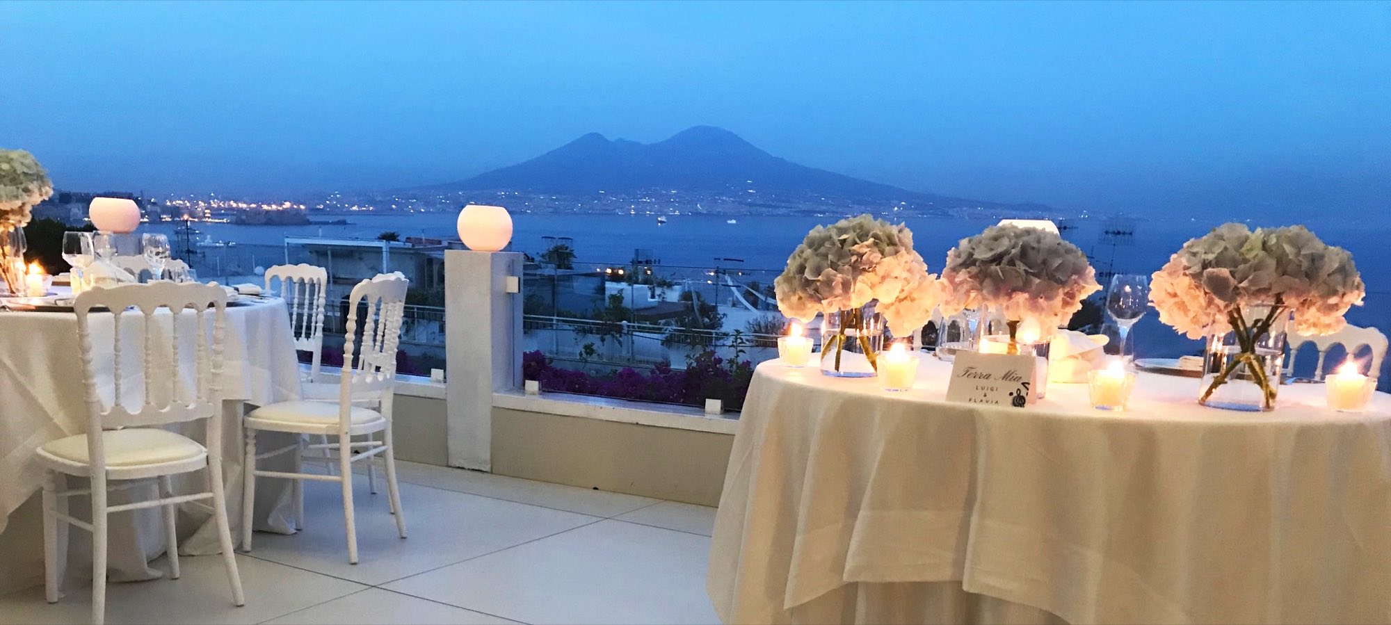 Tavoli allestiti in terrazza al tramonto con il Vesuvio sullo sfondo
